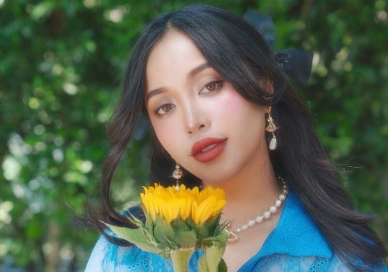 Michelle Phan posing outside with a sunflower for Summer School.