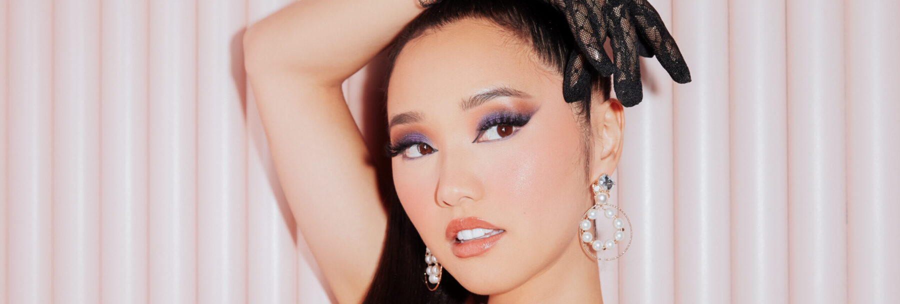 Jenn Im with eye makeup and earrings posing in front of a pick background.